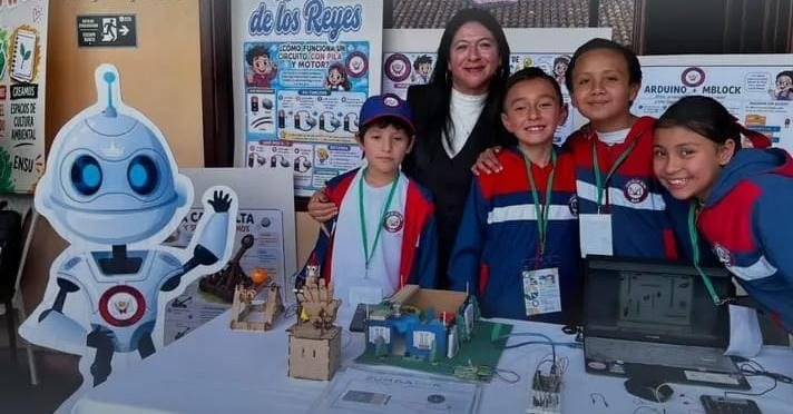 Equipo escolar exhibiendo un proyecto tecnológico en una mesa de exposición